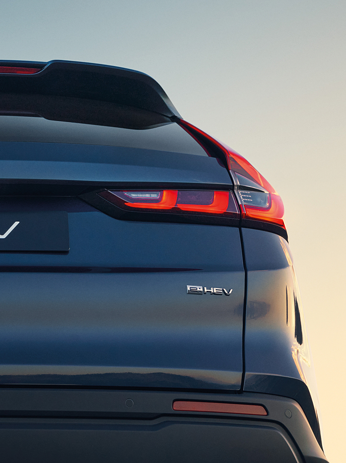 Gros plan arrière d'un Honda CR-V e:HEV Bleu Canyon montrant le badge Honda, le lettrage CR-V et les feux arrière à LED signature illuminés sur un doux ciel de coucher de soleil.