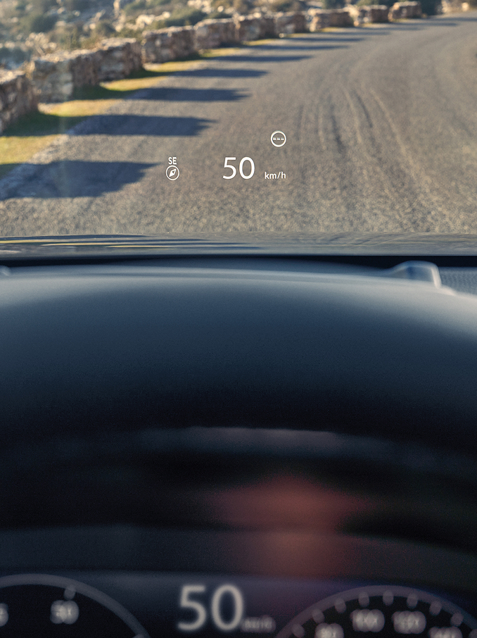 Une vue depuis le siège conducteur montrant un affichage tête haute (HUD) projetant « 50 km/h » et une boussole sur le pare-brise au-dessus d'une route de gravier.