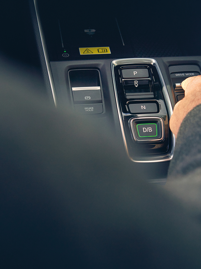 La main d'une personne atteint un commutateur sur la console centrale d'un véhicule moderne, à côté des boutons de sélection de rapport.
