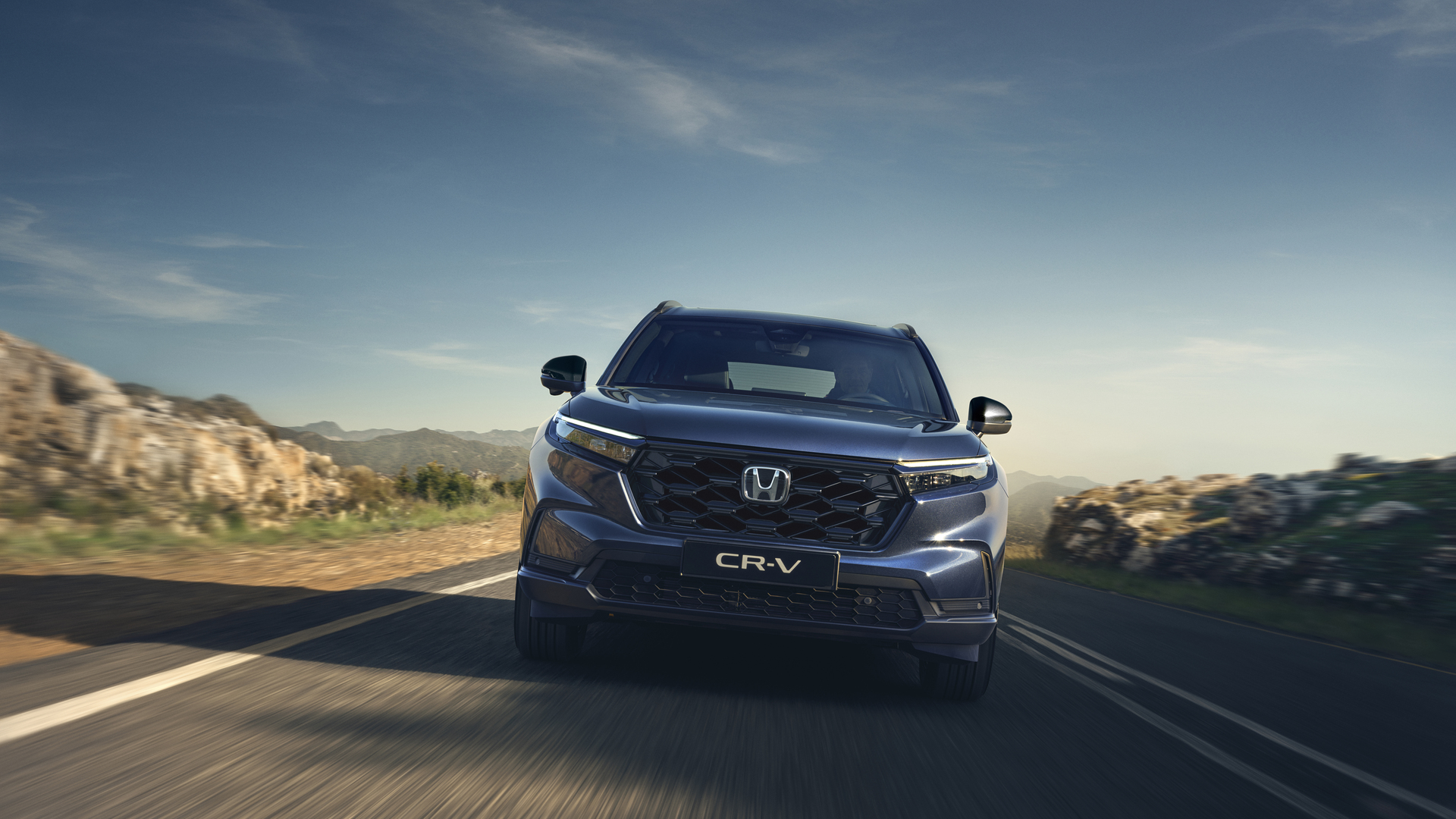 Une Honda CR-V roule sur une route de montagne sinueuse sous un ciel bleu azur.