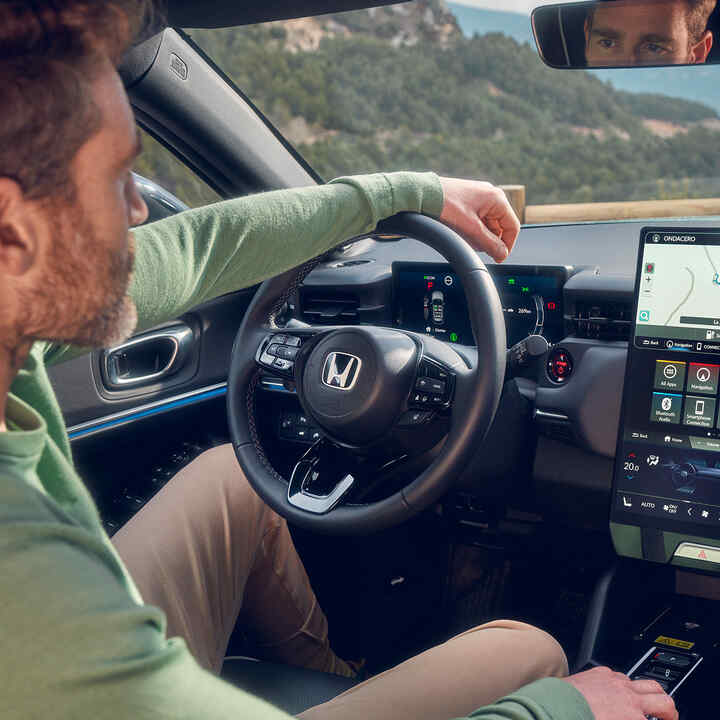 Homme au volant d’un Honda e:Ny1 utilisant le système de navigation sur l’écran numérique conducteur.
