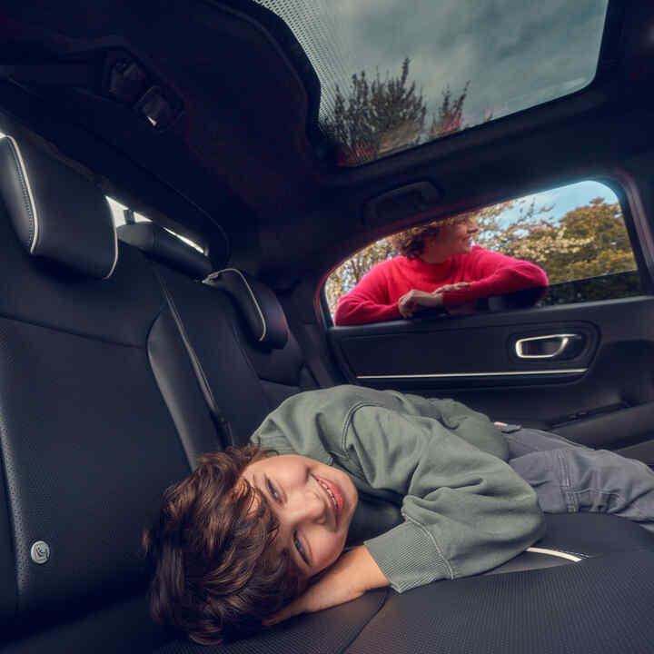 Un enfant allongé sur le siège arrière avec sa mère se tient devant la vitre d’un Honda e:Ny1.