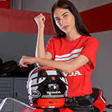 Une femme portant un haut Honda rouge et qui se penche sur un casque de moto Honda.