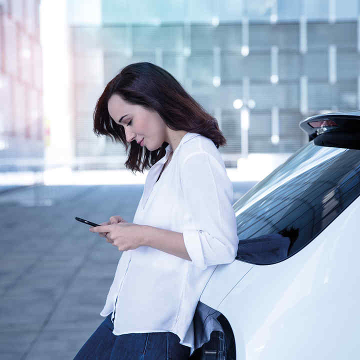 Femme consultant son téléphone, appuyée à l’arrière d’une Honda e