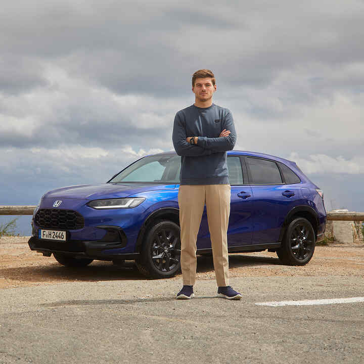 Max Verstappen à côté d'un SUV hybride Honda ZR-V bleu.