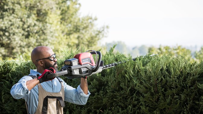 Front-three quarter view of brushcutter with model in a field.