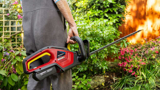 Modèle tenant un taille-haies à batterie Honda dans un jardin.