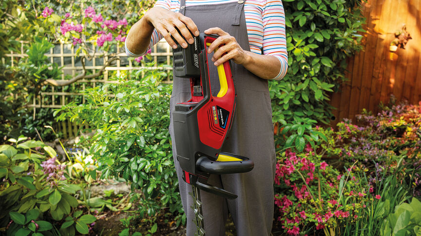 Femme taillant une haie dans un jardin avec un taille-haies à batterie Honda.