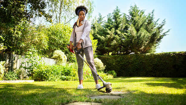 Utilisateur avec un coupe-bordure batterie Honda dans un jardin.