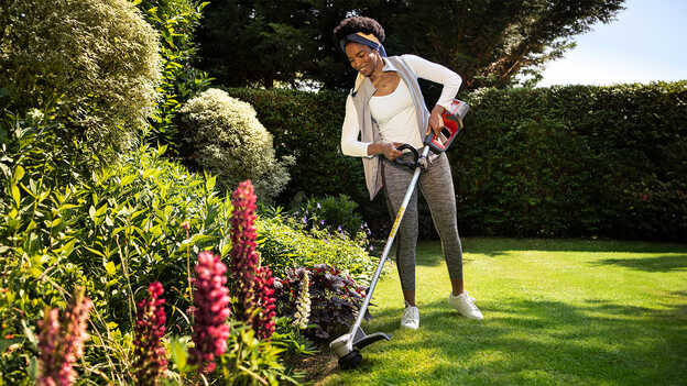 Utilisateur avec un coupe-bordure batterie Honda dans un jardin avec le protège-plante.
