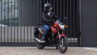 Moto 125 Honda CB125F rouge, trois quarts face, côté droit, conducteur sur la moto arrêtée, dans un environnement urbain