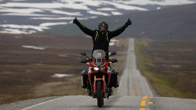 Pilote sur un Honda Africa Twin les bras tendus vers le ciel sur les routes du Cap Nord.