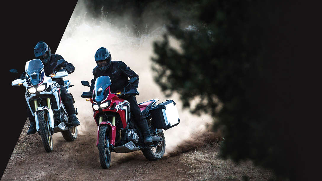 deux Africa Twin roulant sur une piste de terre en forêt