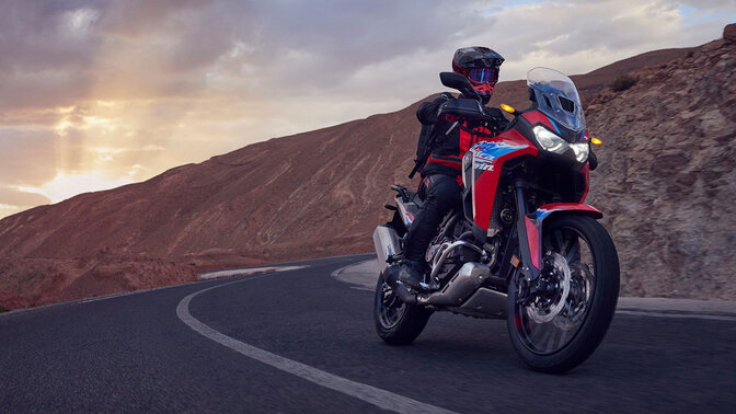 Modèle conduisant une moto CRF1100L Africa Twin sur une route en montagne.