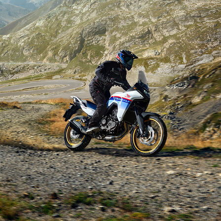 XL750 Transalp sur piste de gravier devant des montagnes.