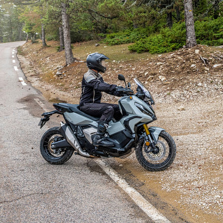 Coté droit de la Honda X-ADV, grise, avec pilote, sur un chemin forestier