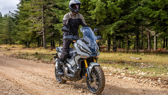 Vue de trois quarts avant droit de la Honda X-ADV, avec pilote, sur une route forestière