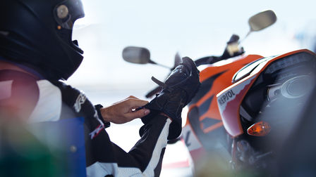 Conducteur ajustant son gant droit assis. Arrière de la moto à droite du conducteur.