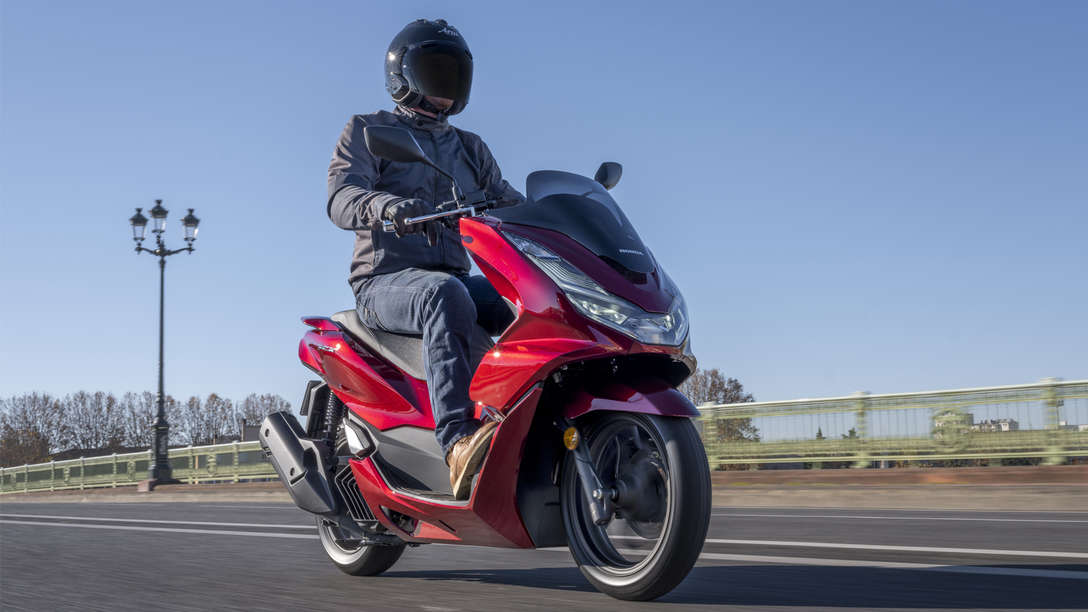 Vue de trois-quart avant droit du Honda PCX125, à l’arrêt, conducteur debout à côté de son scooter gris