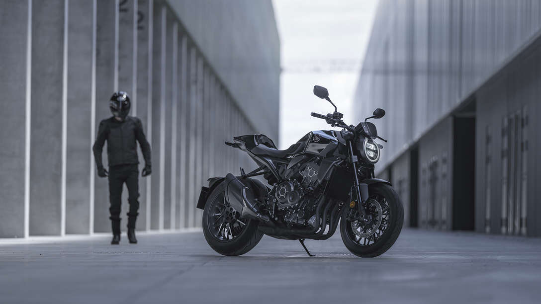 Roadster Honda CB1000R Black Edition - homme se tenant à côté de la moto dans la rue entre deux bâtiments