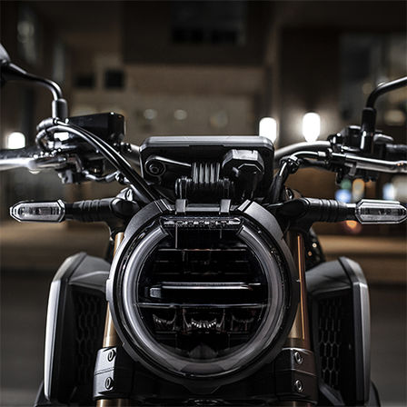 Vue avant du Roadster Honda Permis A2 CB650R Neo Sports Café, gros plan sur le phare avant, la nuit dans un paysage urbain 