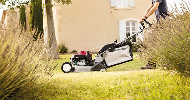 Vue latérale de la tondeuse à gazon Honda HRD avec points de réglage de la hauteur dans un jardin.